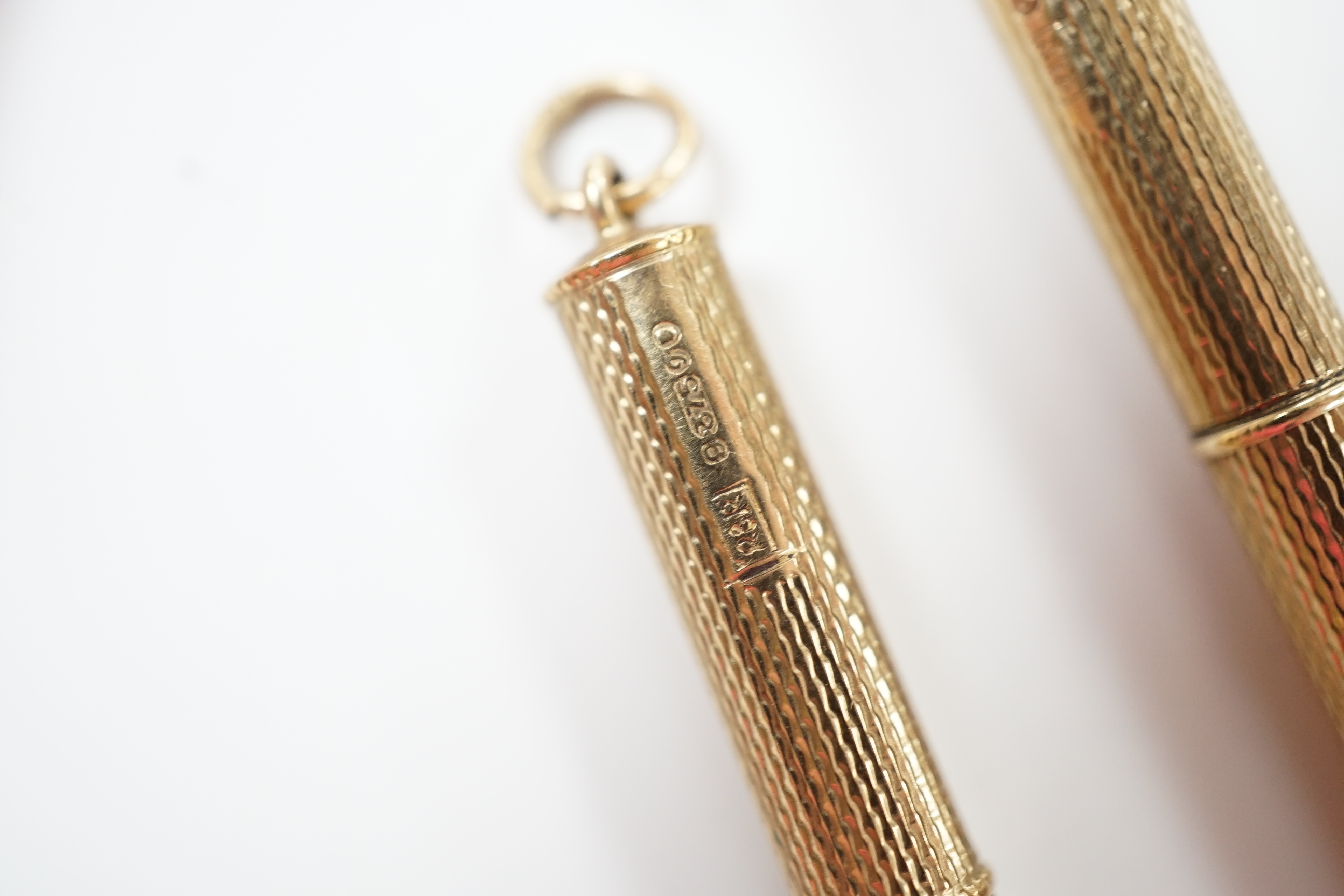 Two engine turned 9ct gold cased propelling toothpicks, 43mm.